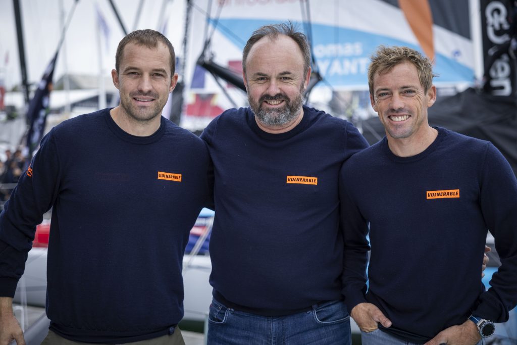 Samuel Goodchild, Alexandre Fayeulle et Thomas Ruyant sourient ensemble sur un ponton avec le t-shirt VULNERABLE